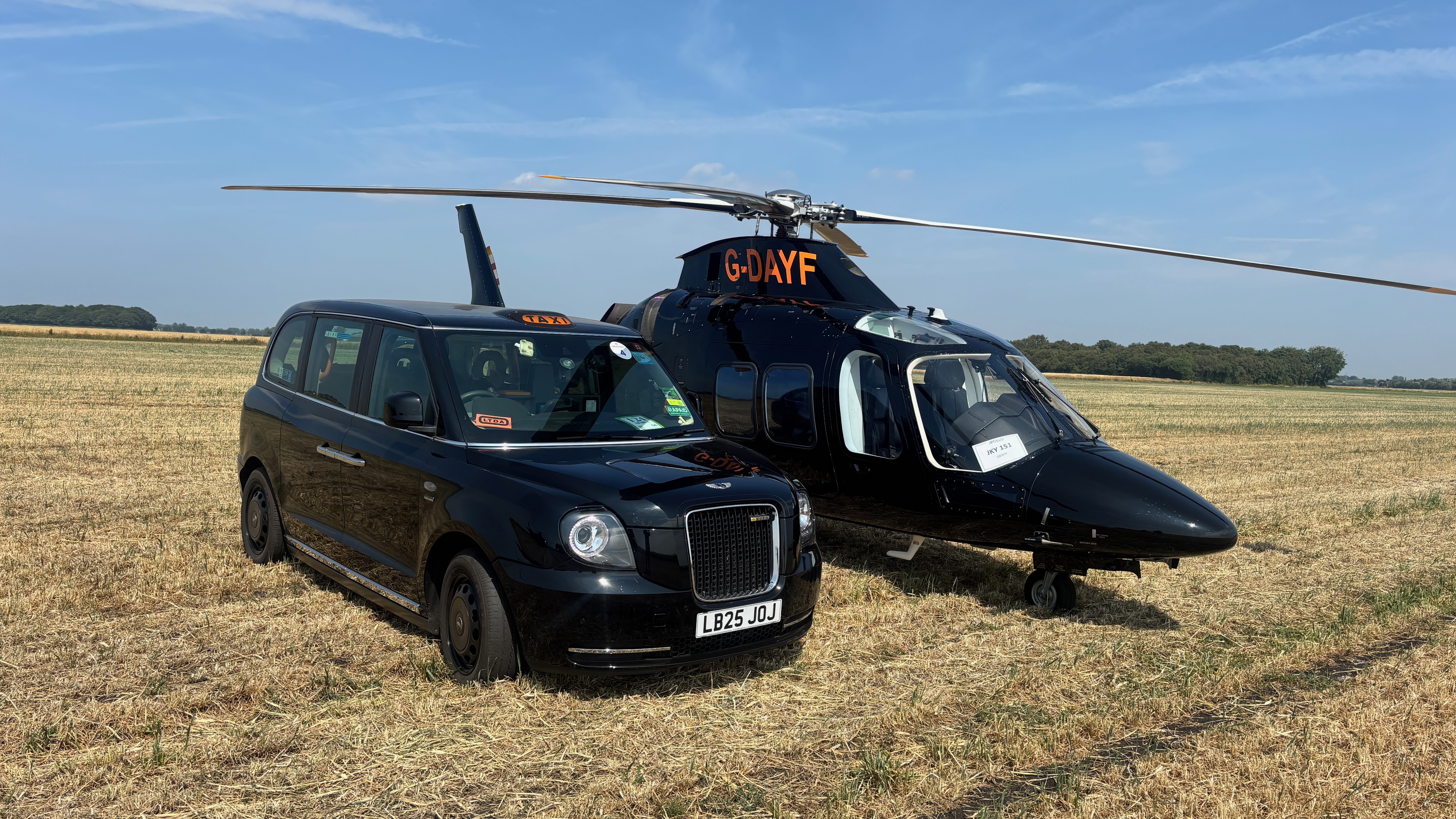 London black taxi beside a helicopter on a grass field